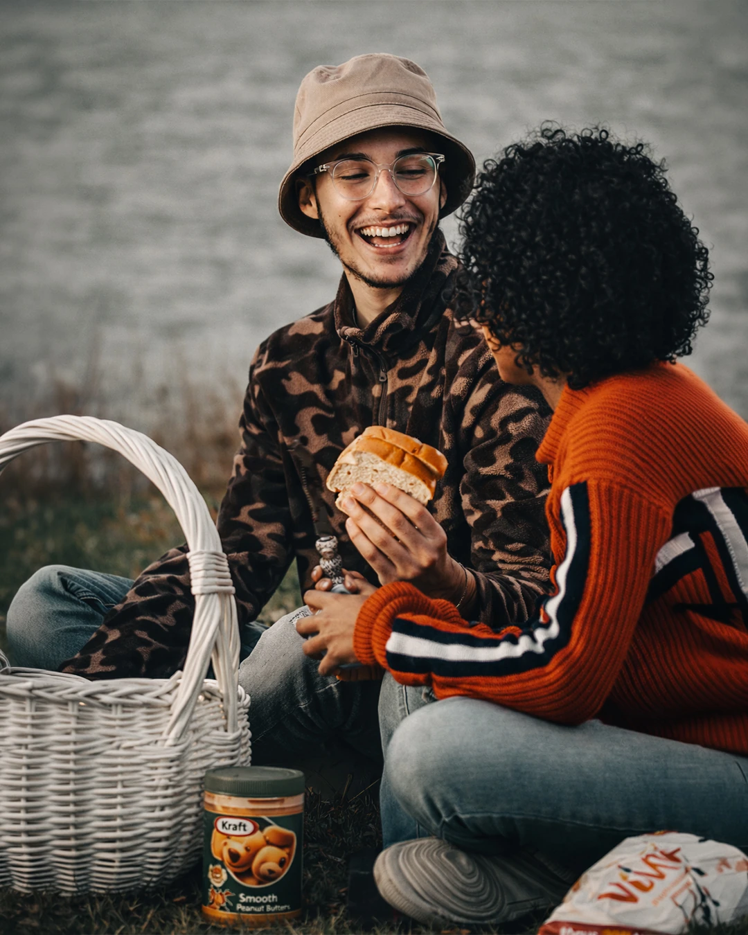 Two people share a smiling moment at a picnic beside a white basket.