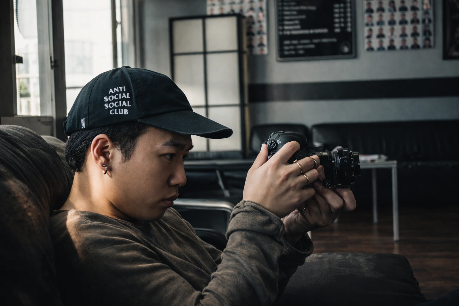A person in a black baseball cap studies a camera while seated indoors.