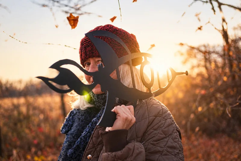 Eine Frau mit roter Strickmütze und Steppjacke hält im hellen Gegenlicht einen schwarzen ornamentalen Ausschnitt vor ihr Gesicht.