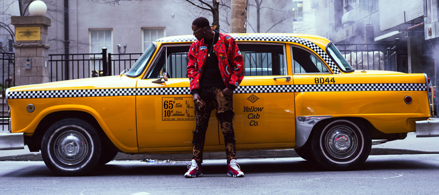 Concrete Rhythms A stylish man in a red patterned jacket leaning against a classic yellow taxi cab on a city street.