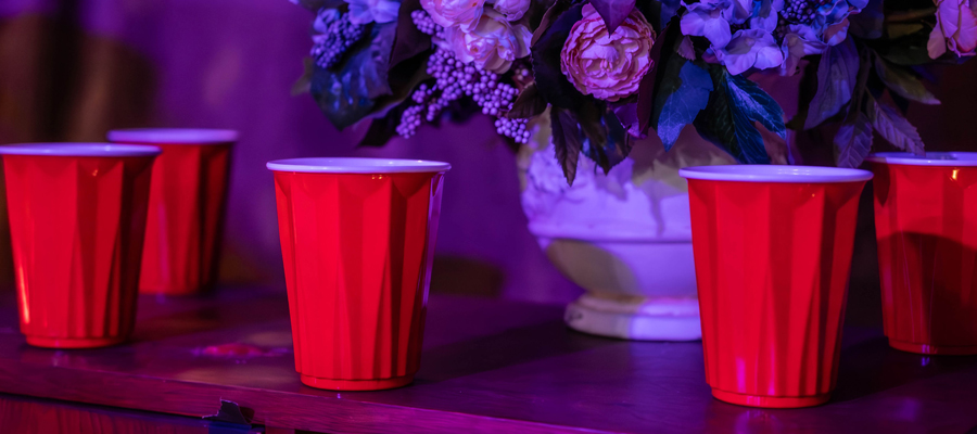 Neon Nostalgia Red plastic cups lined up on a surface under purple party lighting next to an elegant floral arrangement.