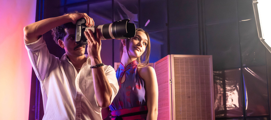 Editorial Vision A creator holding a large lens camera taking a portrait of a female model in a vibrant, colorfully lit studio space.