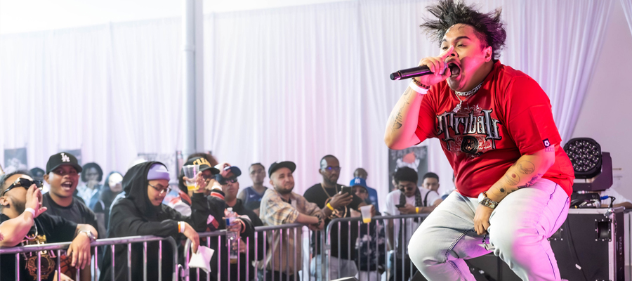 Elevated Energy A musical artist jumping energetically on stage while singing into a microphone, with a crowd watching behind the barricade.