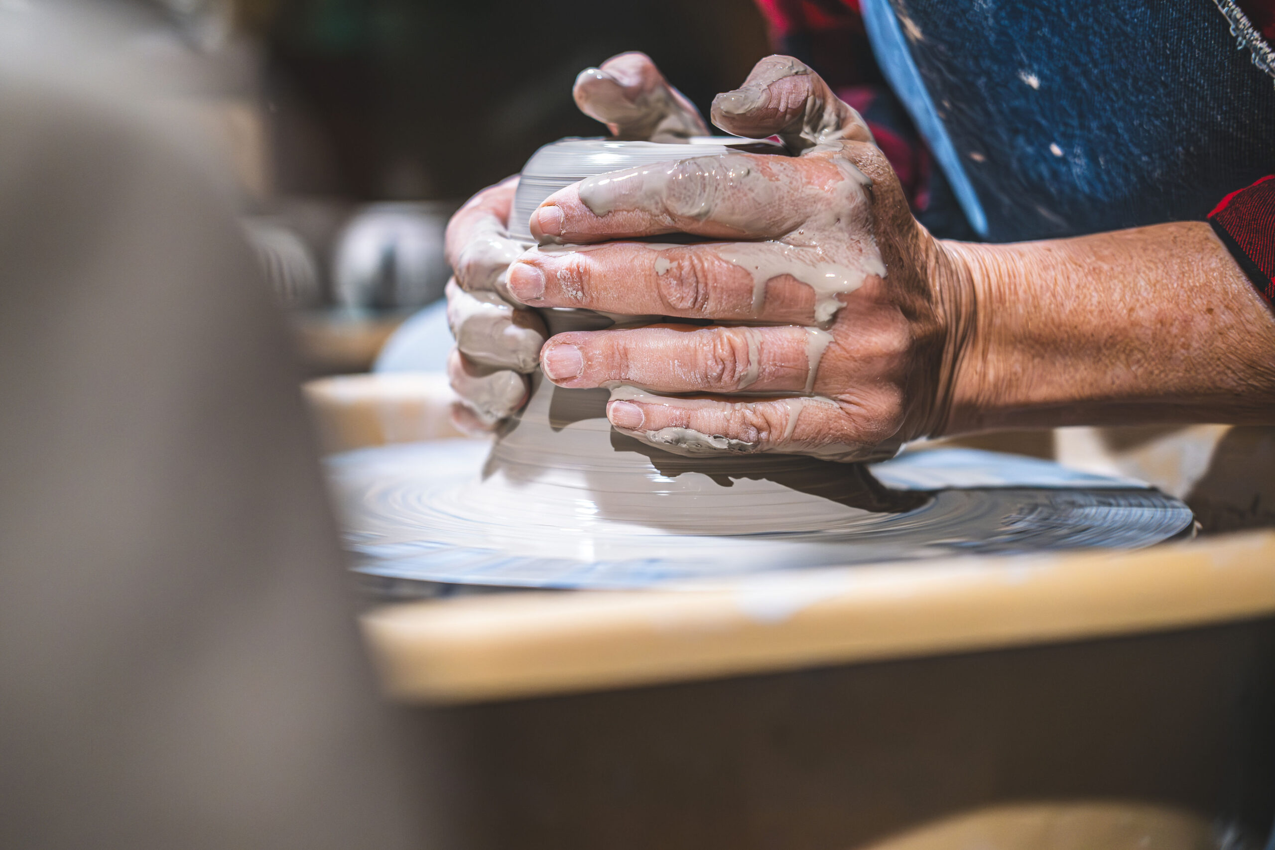Close-up of an artisan's wet, clay-covered hands shaping a ceramic bowl on a spinning pottery wheel.