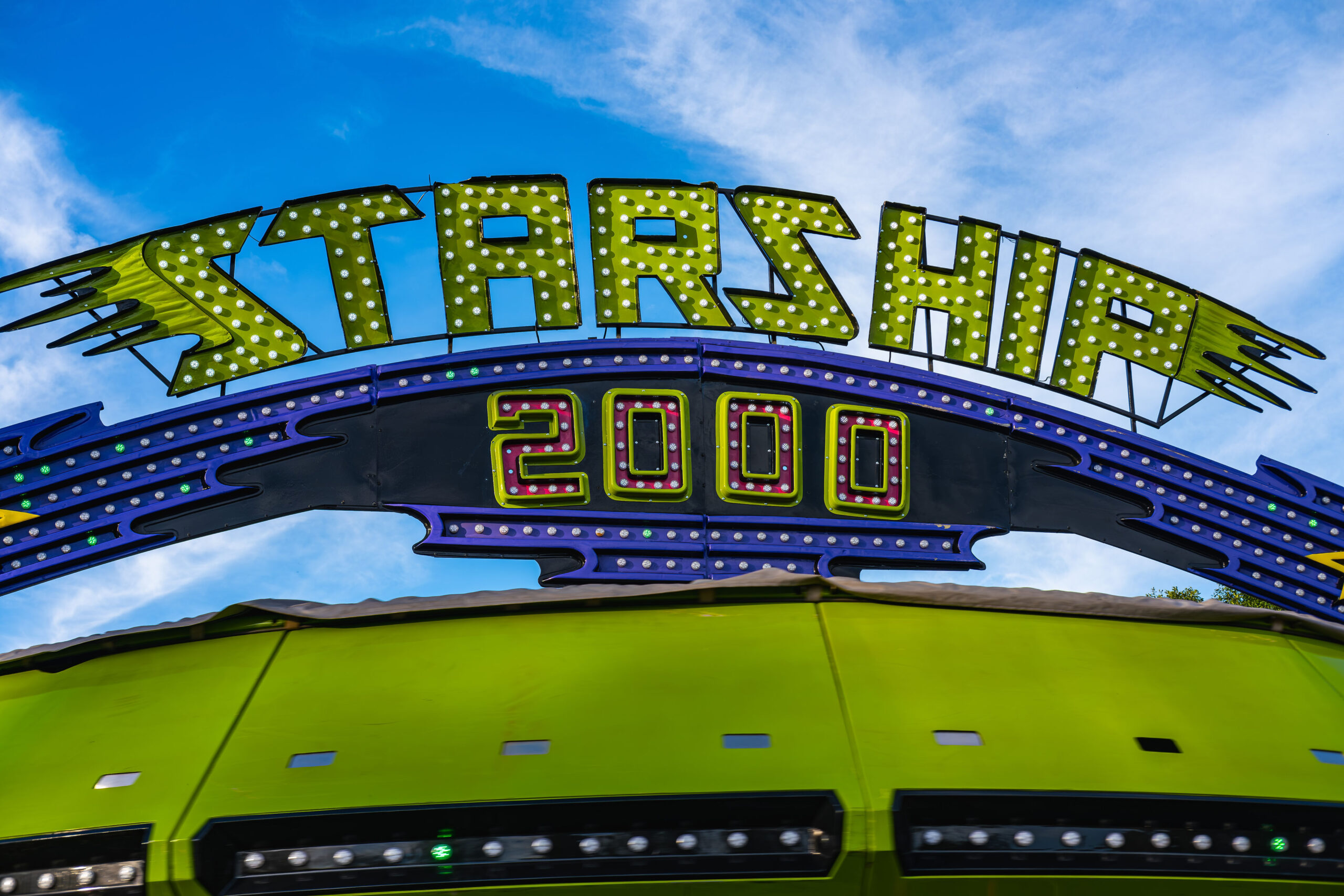 A neon sign reading STARSHIP 2000 above a green carnival ride under a bright blue sky.