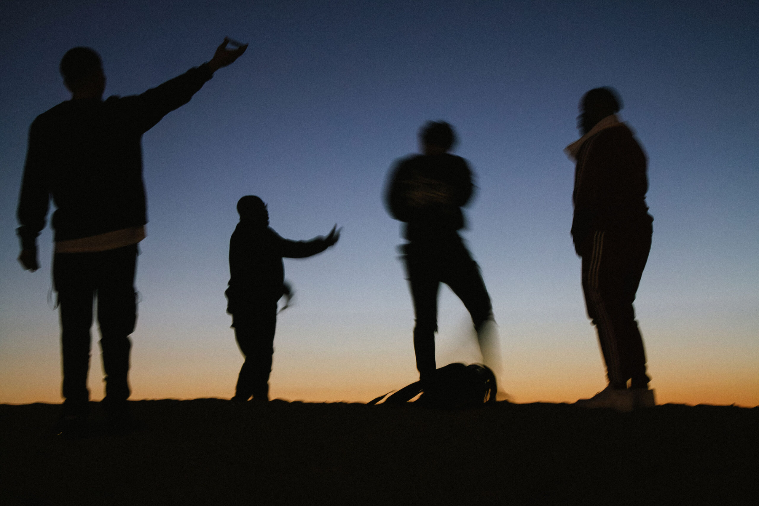 Silhouettes of four people standing together outdoors against a smooth, gradient twilight sky of dark blue and orange.