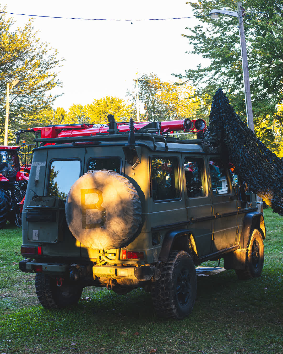 A custom matte green Mercedes G-Wagon parked on a grassy field illuminated by warm golden hour sunlight.