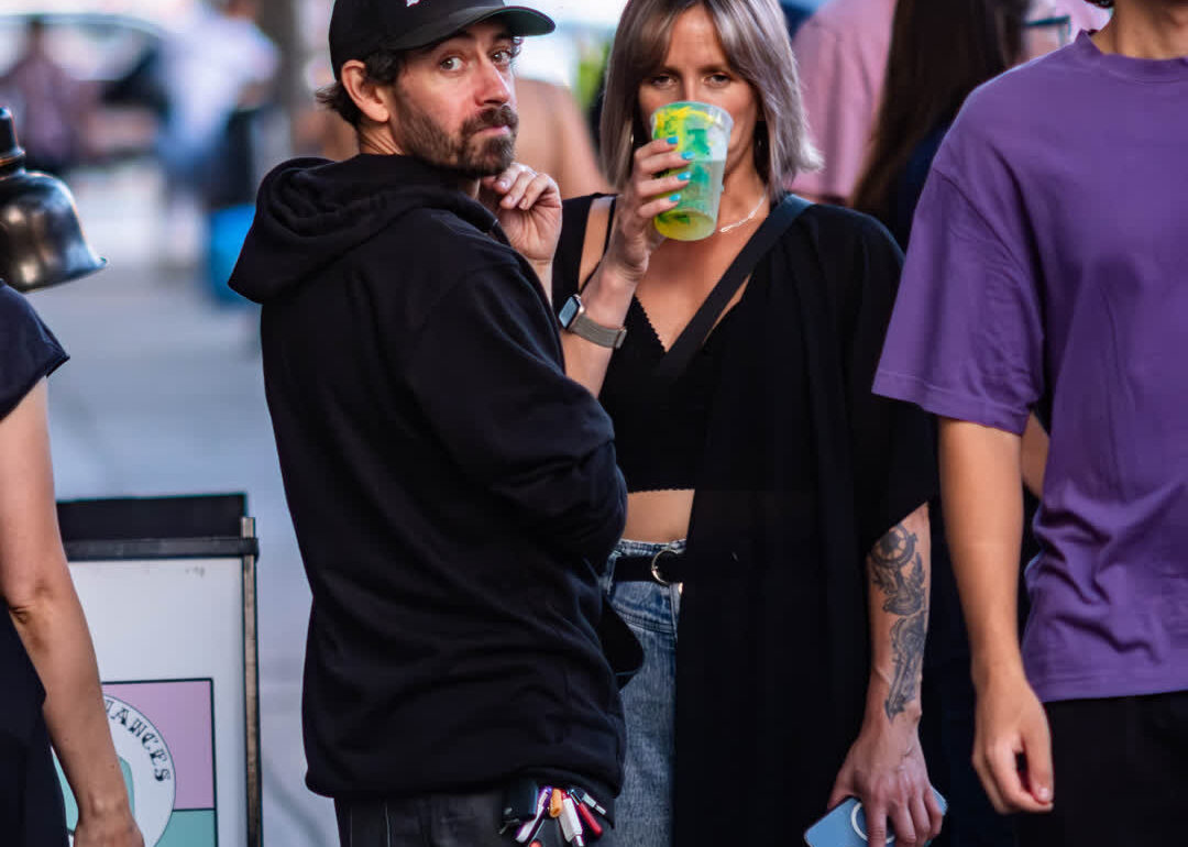 Candid street photography of a man in a black hoodie looking back at the camera while a woman next to him takes a drink from a plastic cup.
