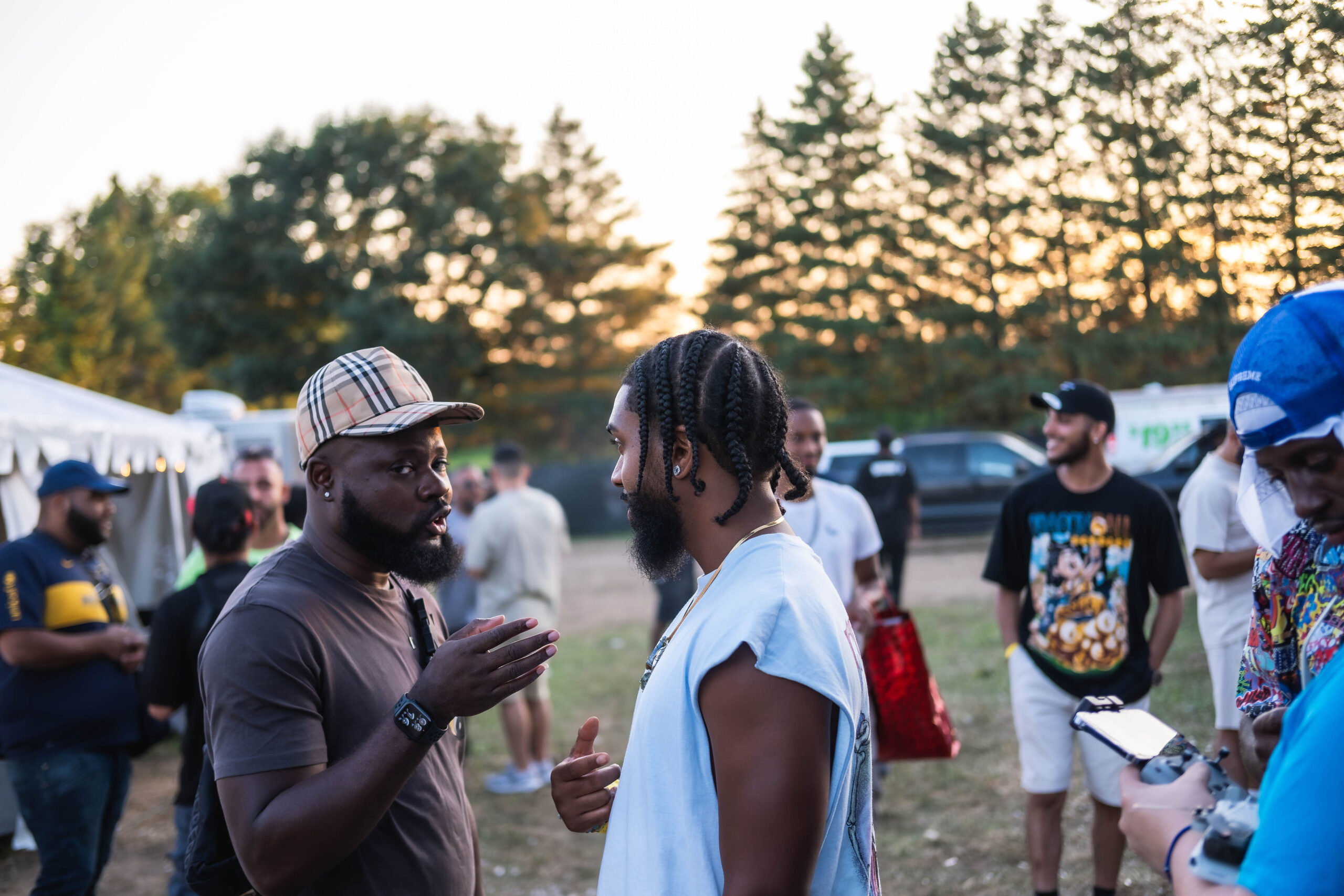 Candid portrait of two men talking intimately at an outdoor event, surrounded by a soft-focused crowd in the background at sunset.