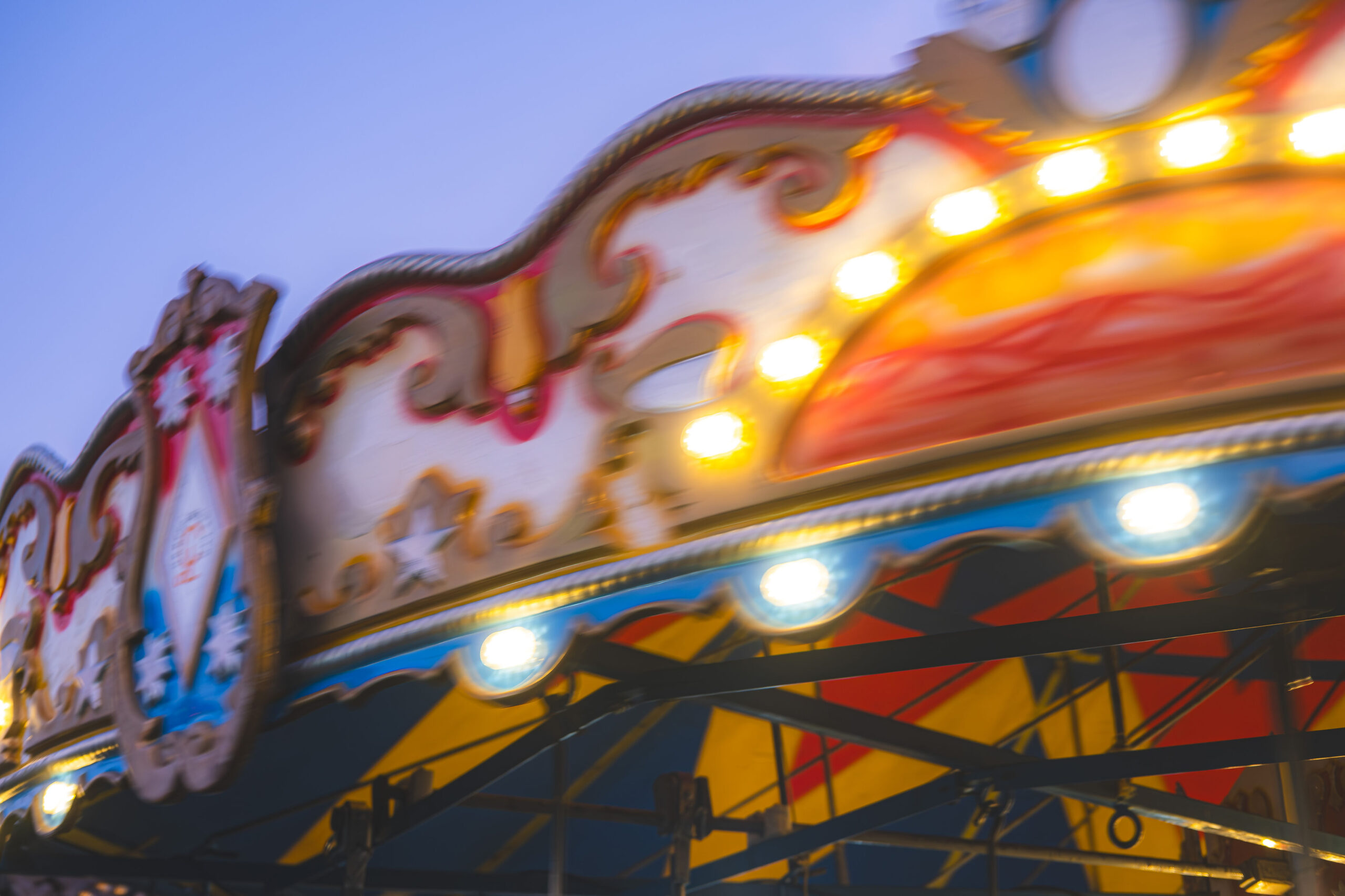 A motion-blurred, long-exposure photograph of a brightly lit amusement park carousel spinning against a twilight sky.