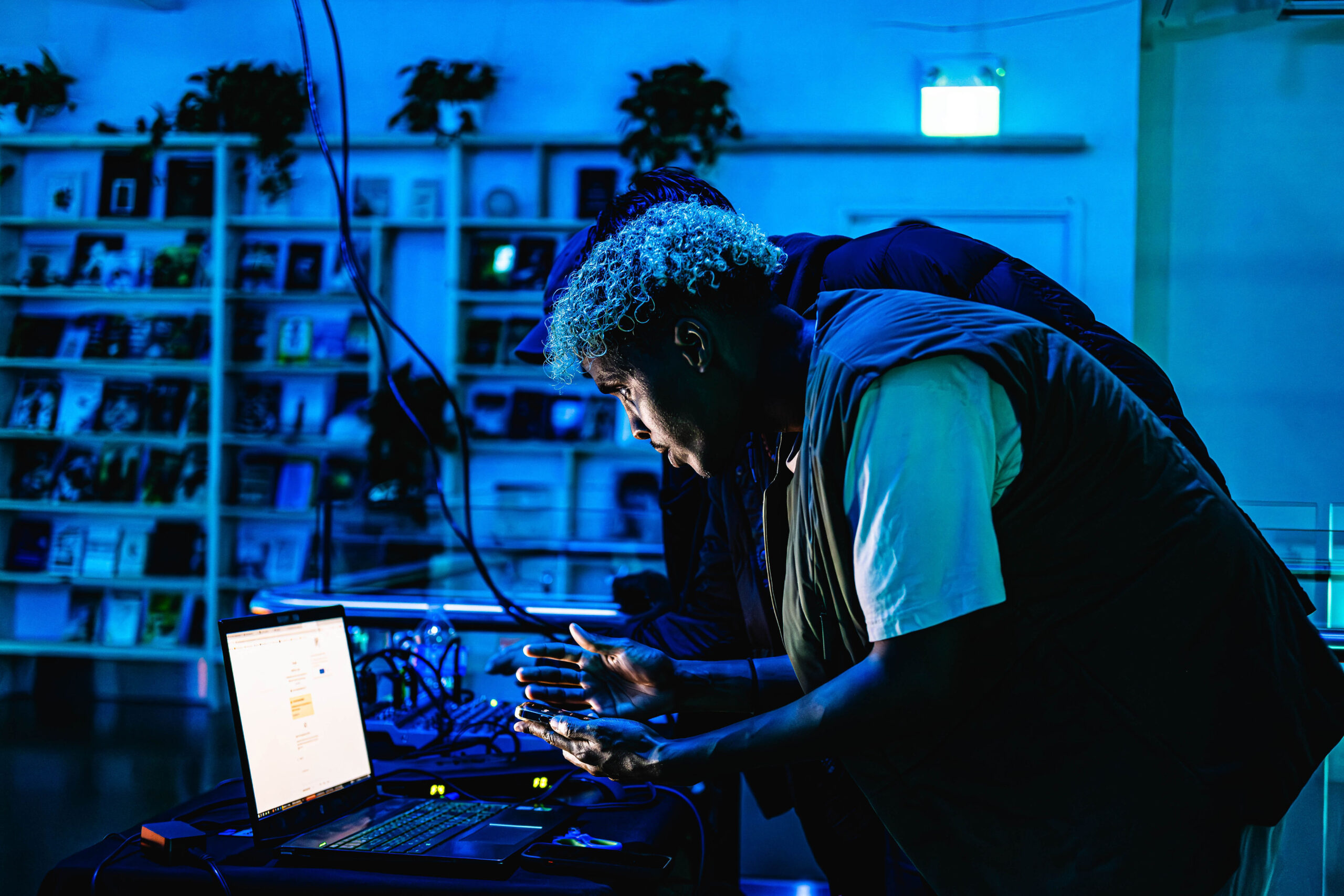 Two creatives illuminated by the glow of a laptop screen, intensely focused on their work in a dark room bathed in atmospheric blue ambient light.