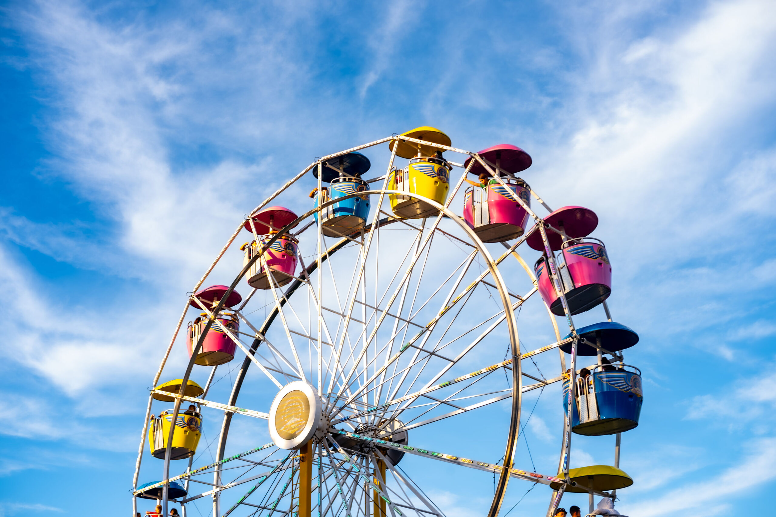 Colorful Ferris wheel cars against a vibrant blue sky with light, wispy clouds.