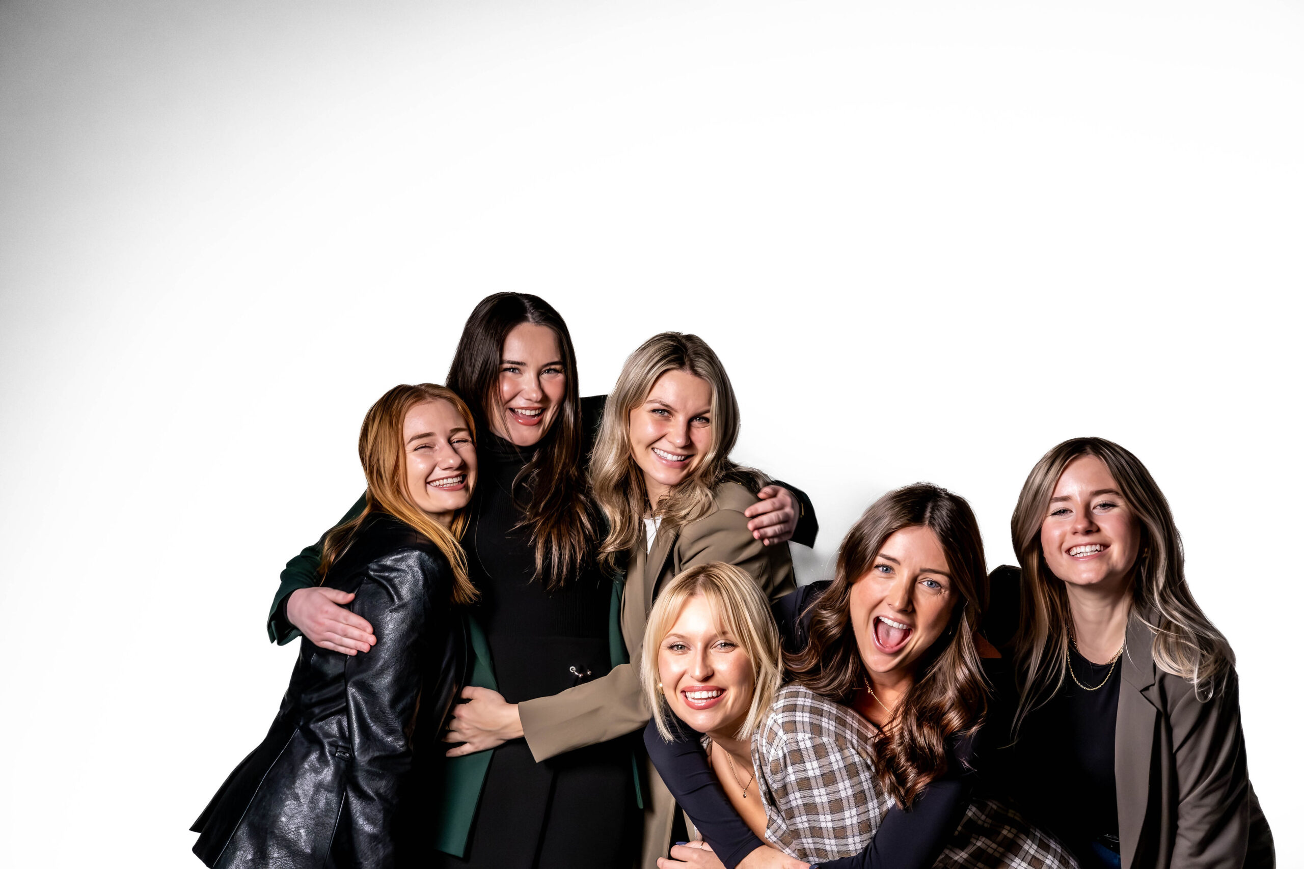 Group of six female friends laughing and embracing together against a solid white studio background.