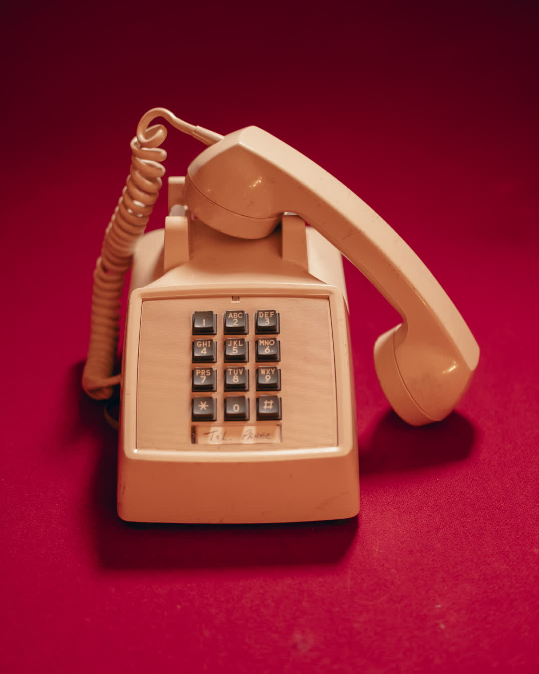 Vintage beige push-button telephone resting off the hook against a vibrant, saturated red background.
