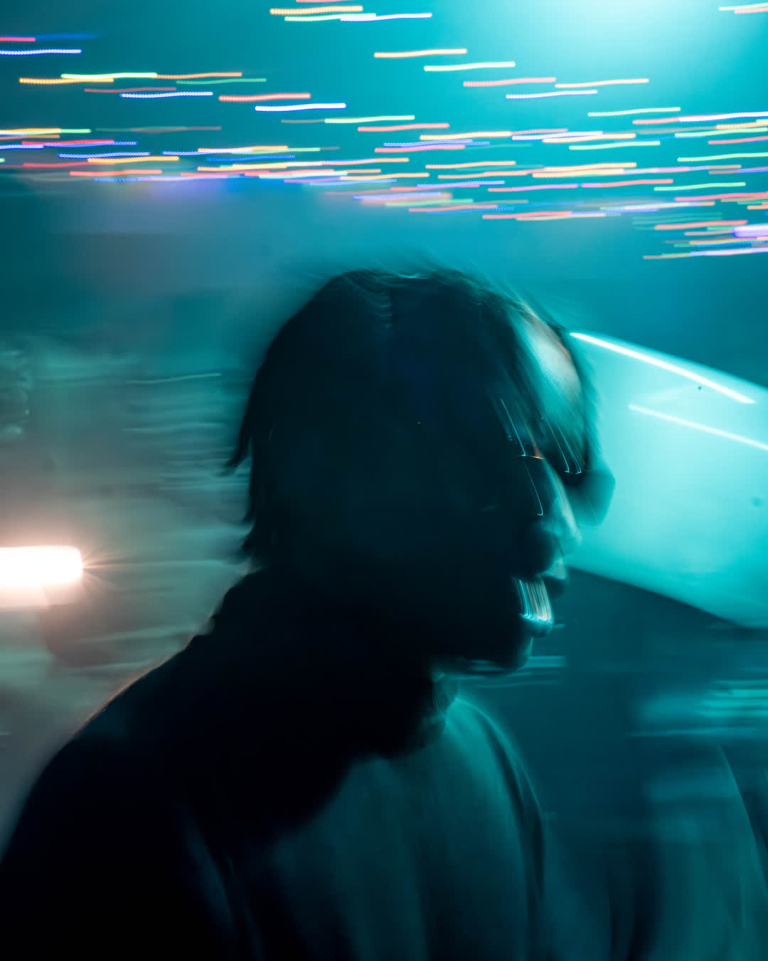 Abstract motion blur photography of a person’s silhouette against glowing, trailing cyan and teal neon lights in a dark, energetic venue.