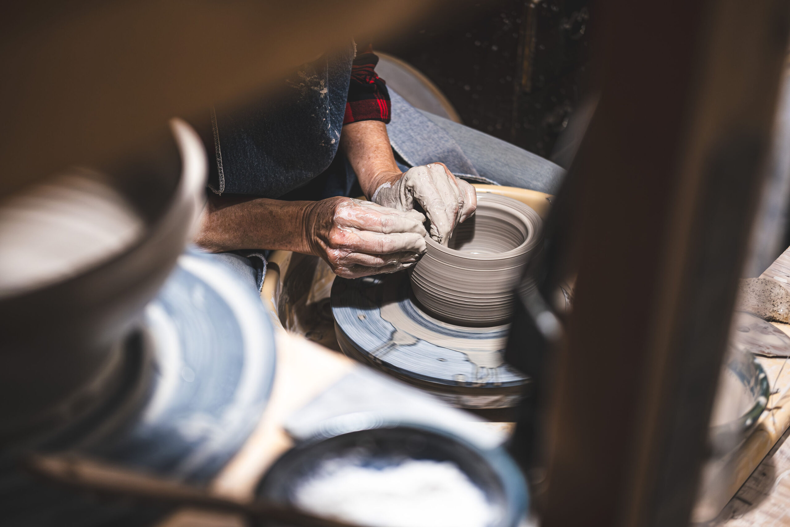 Close up shot of an artisan's muddy hands shaping a wet clay pot on a spinning pottery wheel in a warm, dimly lit workshop.