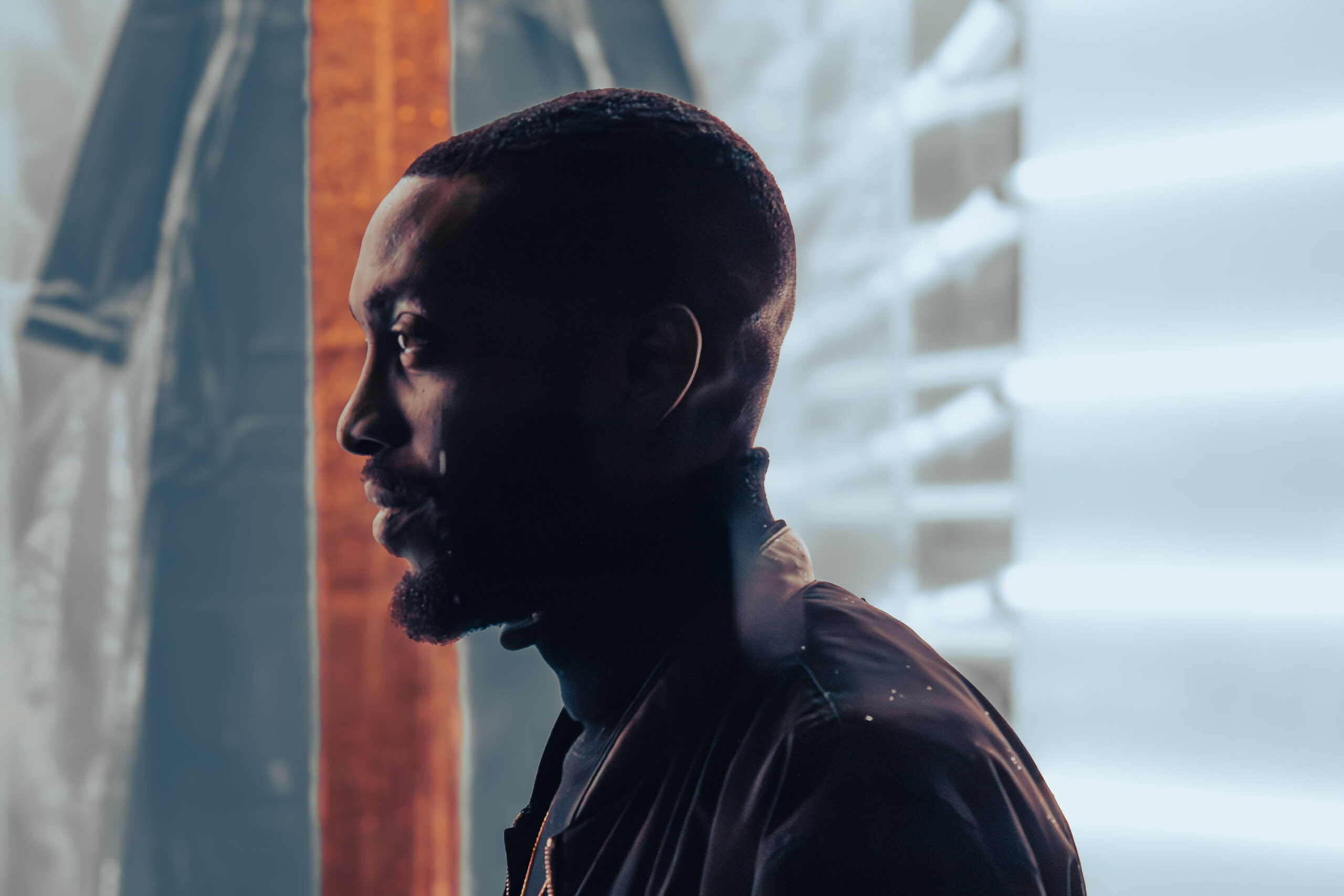 Cinematic profile portrait of a Black man with a beard looking away, illuminated by moody blue and bright white vertical lights.