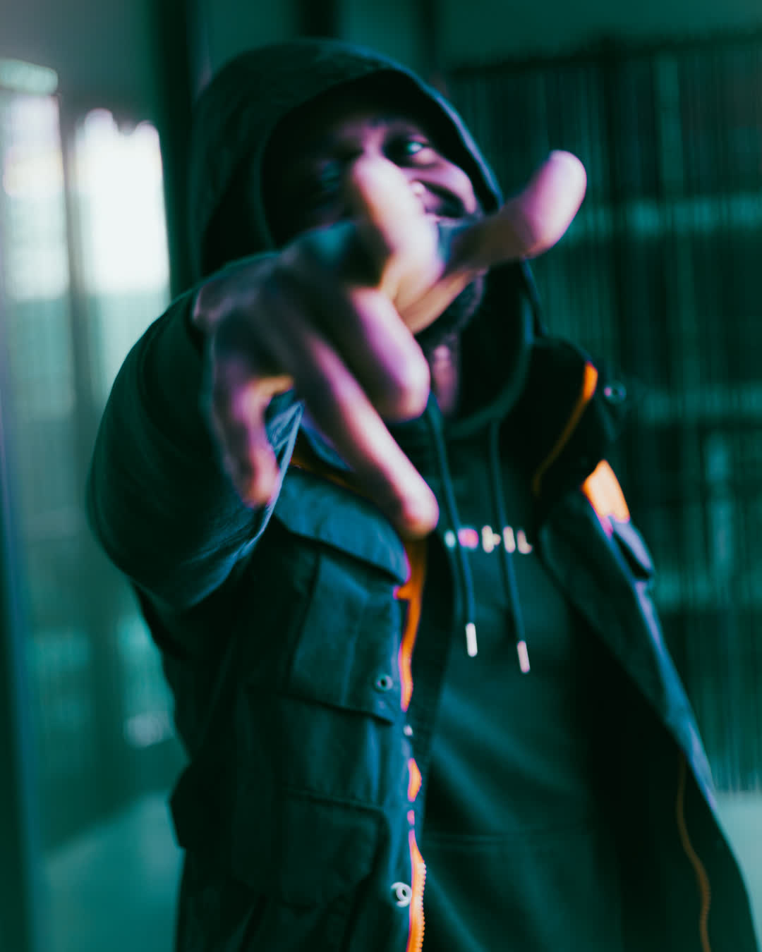 Person in a dark jacket reaching a hand directly out toward the camera lens, illuminated by vibrant teal and orange neon lighting.